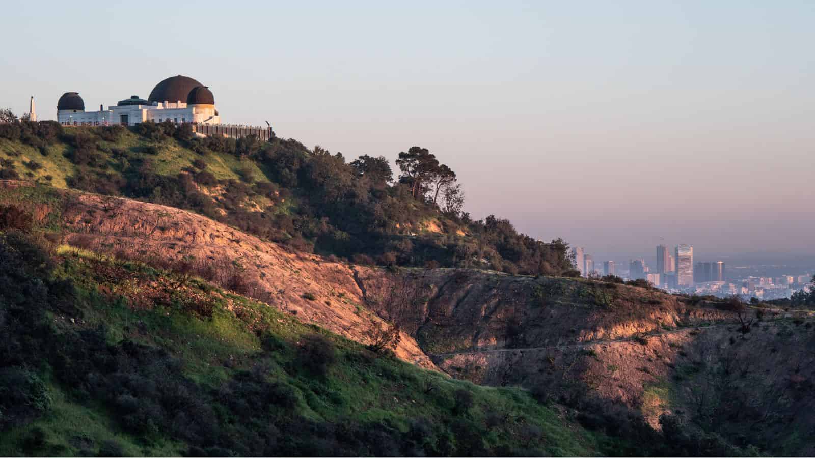 The Griffith Observatory on a hill at sunset, with a city skyline in the background.