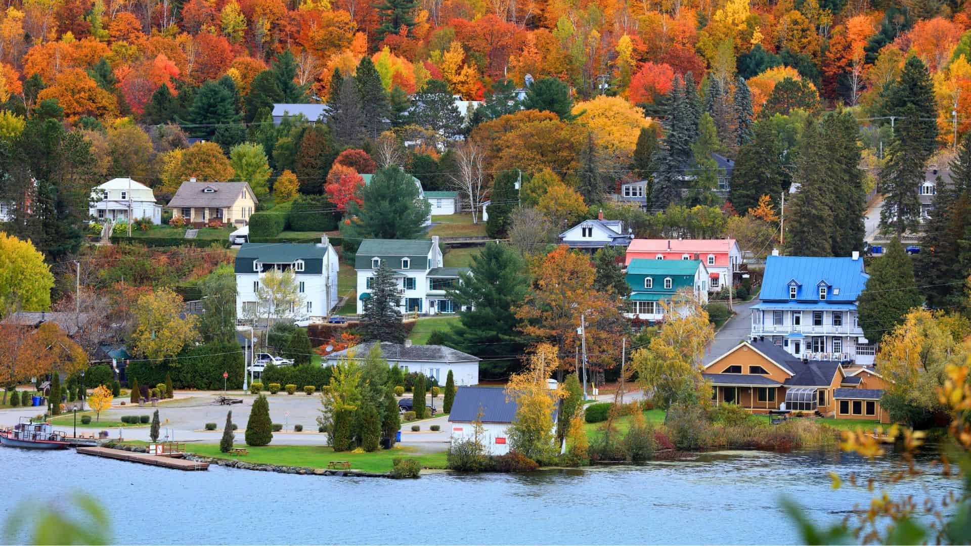 Colorful houses by a lake surrounded by vibrant autumn trees and foliage in a small, scenic village.
