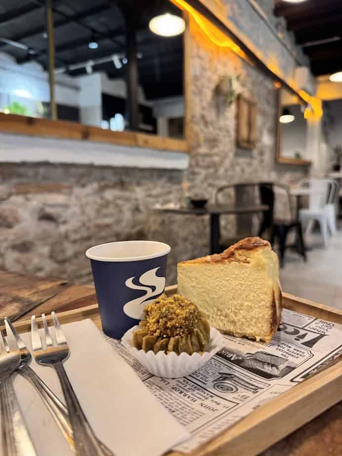 A tray with cheesecake, a pistachio sweet, and coffee on a table in a cozy café—perfect for those exploring where to eat after browsing the vibrant Barcelona markets.
