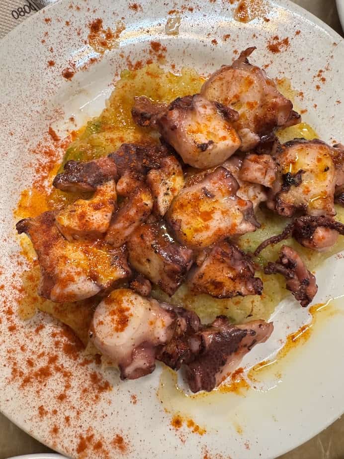 Grilled octopus pieces on a white plate, drizzled with oil and sprinkled with red paprika—a delicious example of fresh food you’ll often find at Barcelona markets.