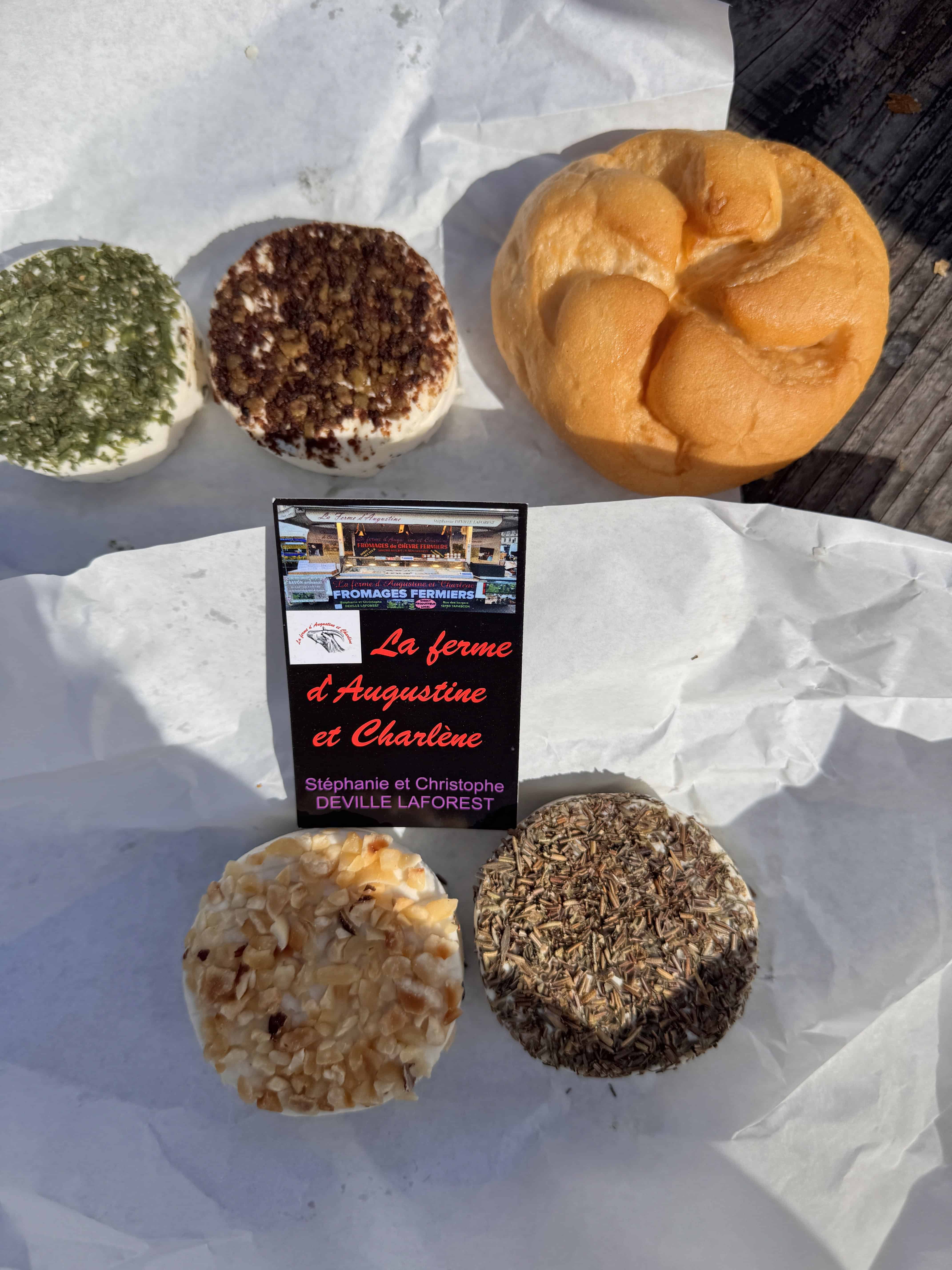 Four types of cheese and a bread roll on parchment paper, with a business card for a local cheese farm—perfect for adding a taste of France to your Marseille itinerary.