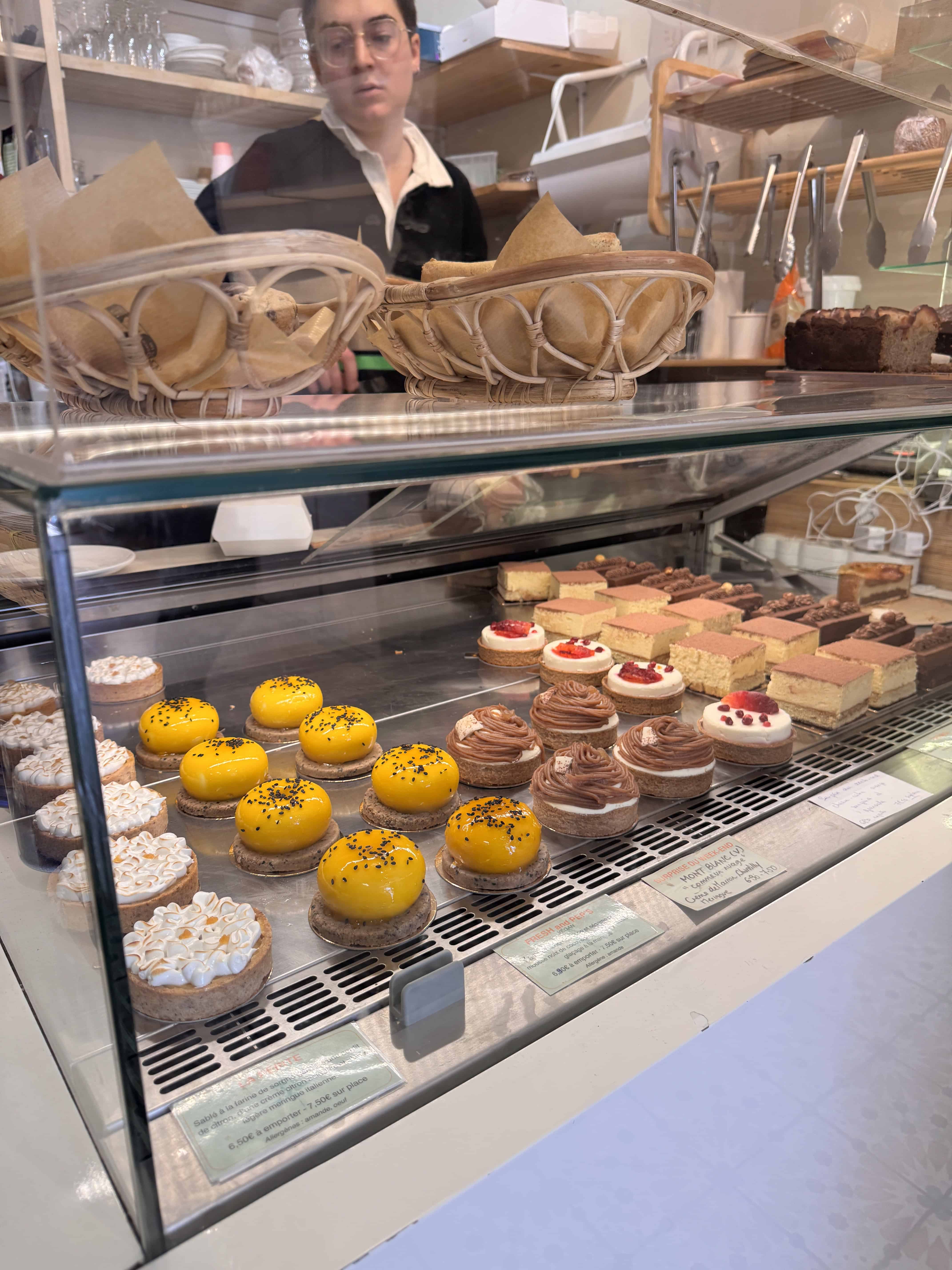 A bakery display case with colorful pastries and a person standing behind the counter, evoking the charm of France—perfect for adding to any Marseille itinerary.