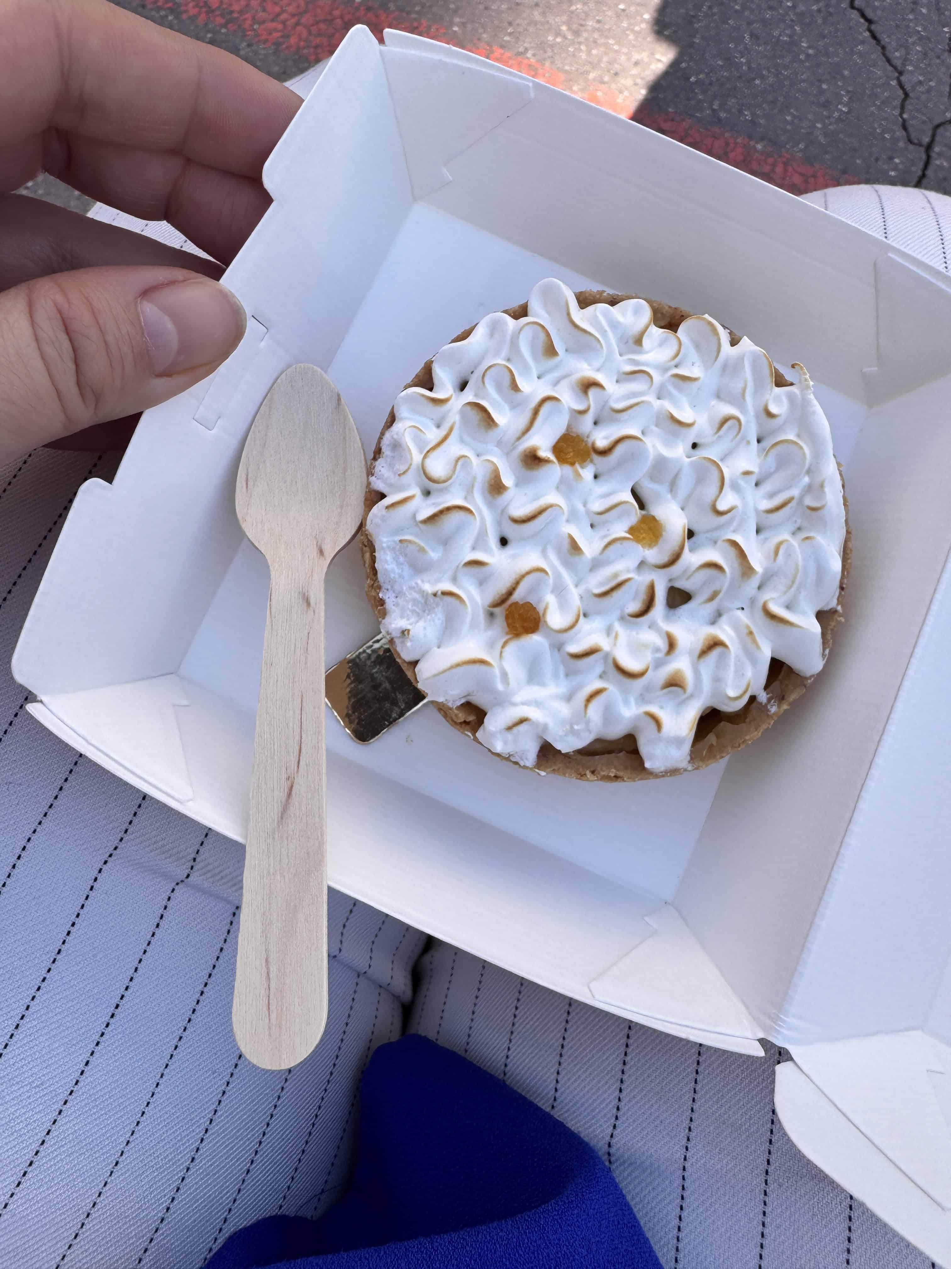 A hand holds an open box with a mini pie topped with meringue and a small wooden spoon inside—perfect for enjoying a sweet treat while exploring an itinerary through Marseille, France.