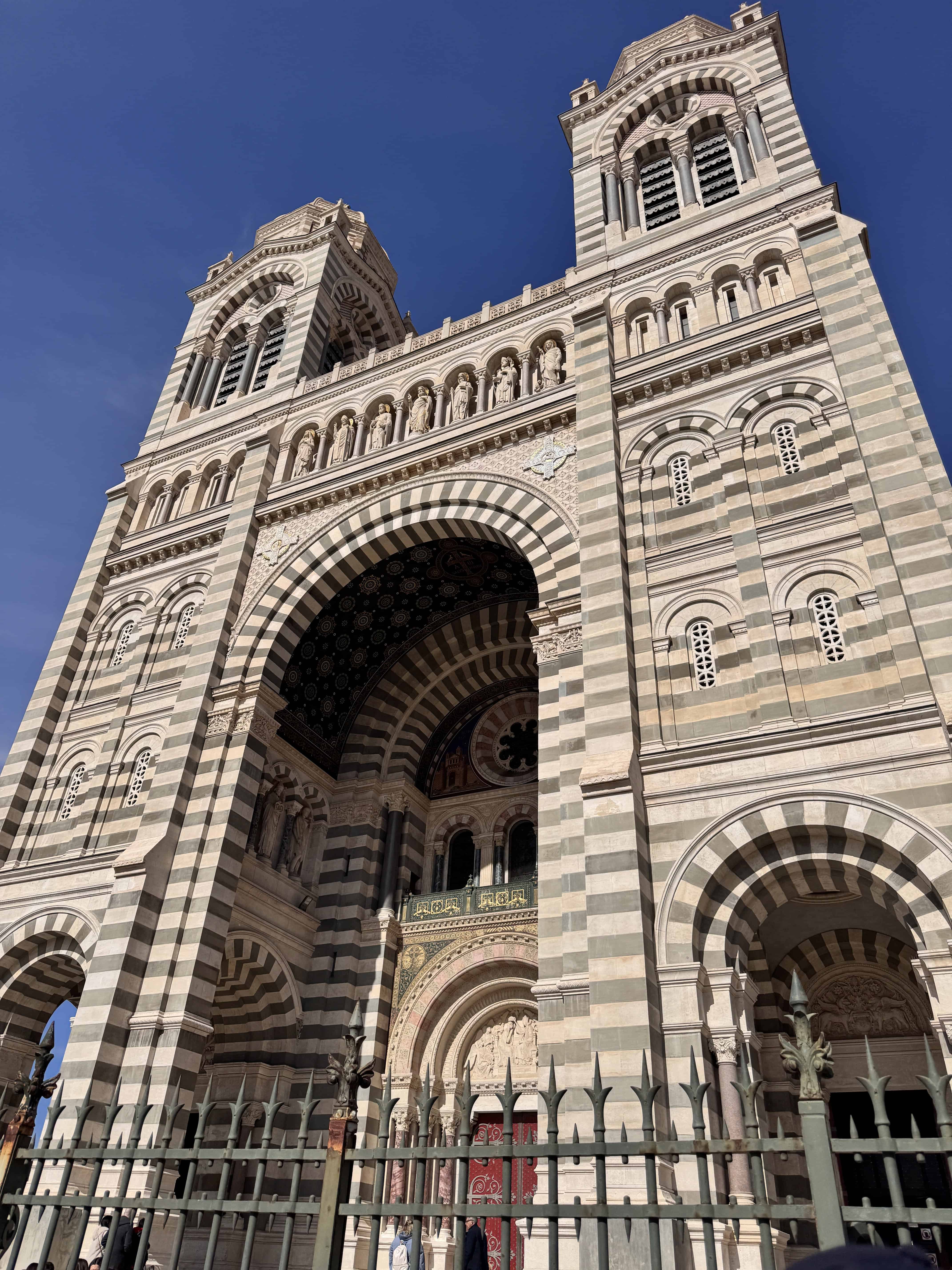 Striped stone façade of a grand cathedral with arches and twin towers under a clear blue sky—a must-see on any Marseille itinerary in France.