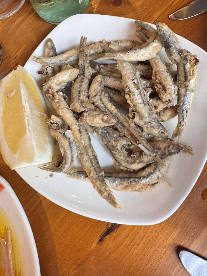 A plate of fried small fish served with a wedge of lemon on a wooden table—enjoy this fresh food at one of the vibrant Barcelona markets.