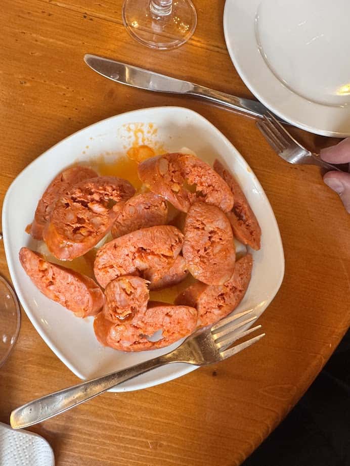 Sliced chorizo sausages on a white plate with a fork and knife on a wooden table, capturing the vibrant flavors of fresh food inspired by Barcelona markets.