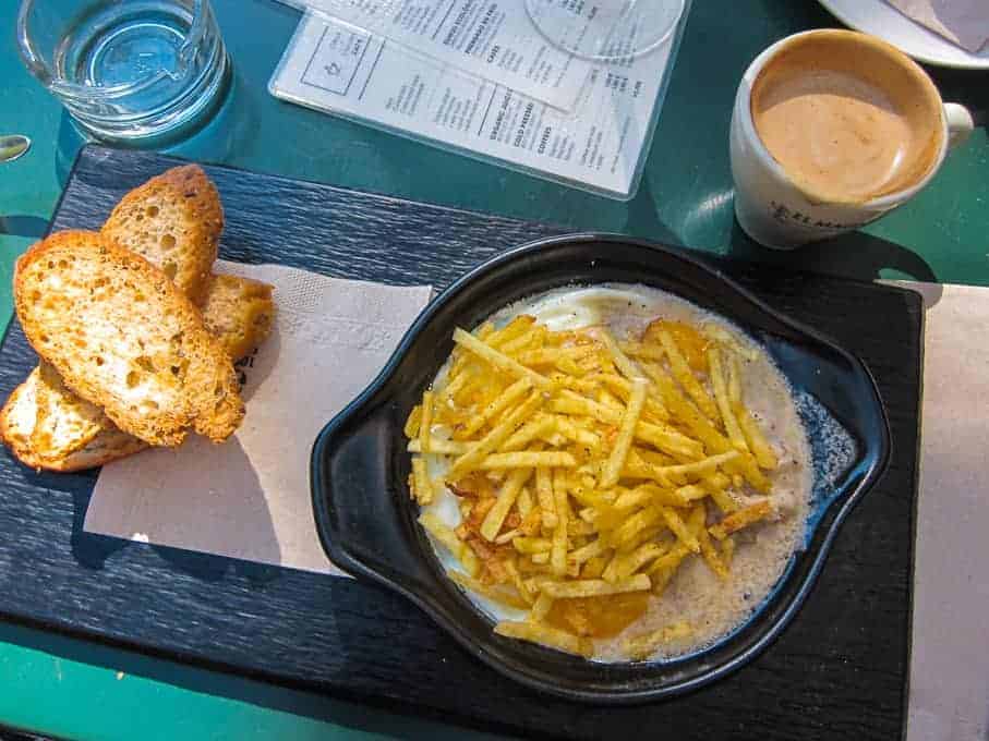 A dish of melted cheese topped with shoestring fries, toasted bread slices, and a cup of coffee on a tray.