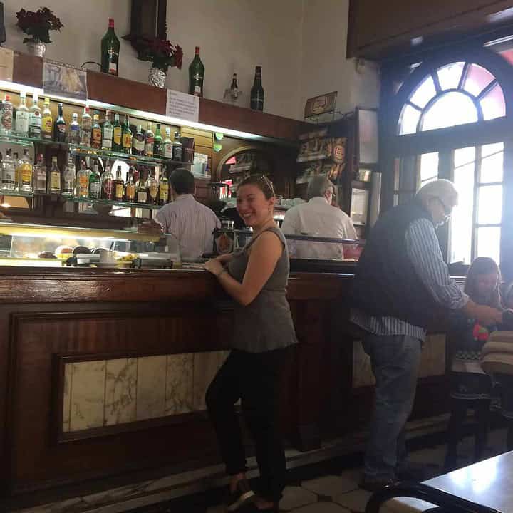 Woman smiling at a bar counter inside a cozy café with people in the background.