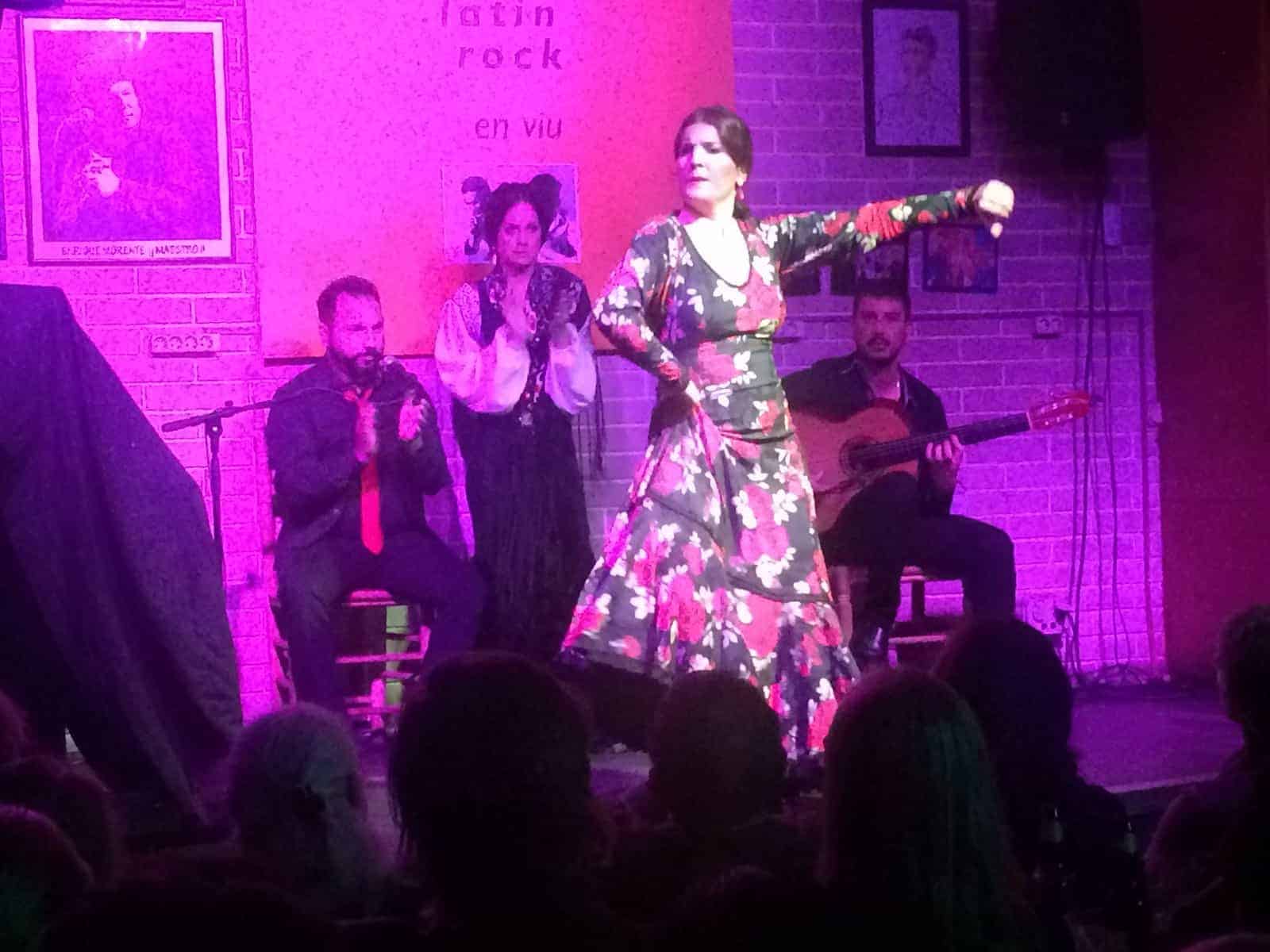 A woman performs flamenco dance on stage as musicians and a singer accompany her in the background.