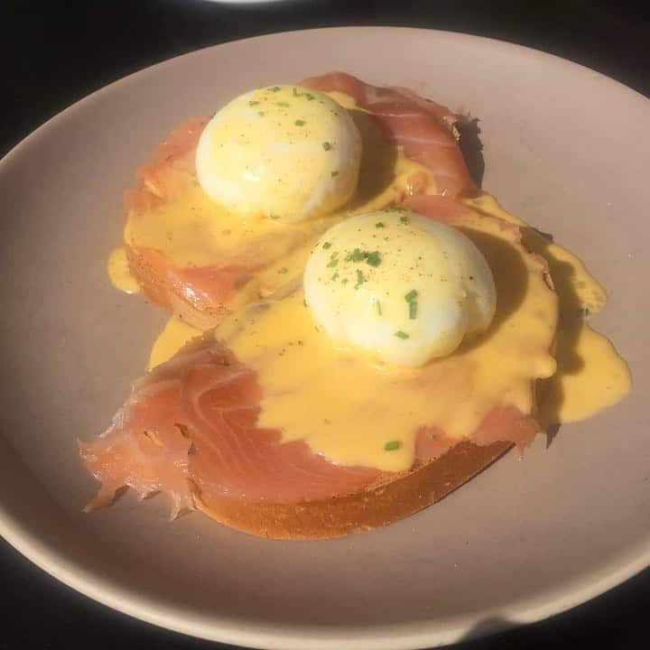 Two slices of bread topped with smoked salmon, poached eggs, and creamy hollandaise sauce on a plate.