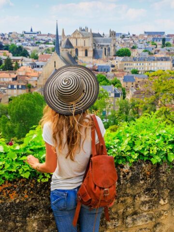 Charming woman with a sun hat overlooking historic European cityscape with lush greenery.
