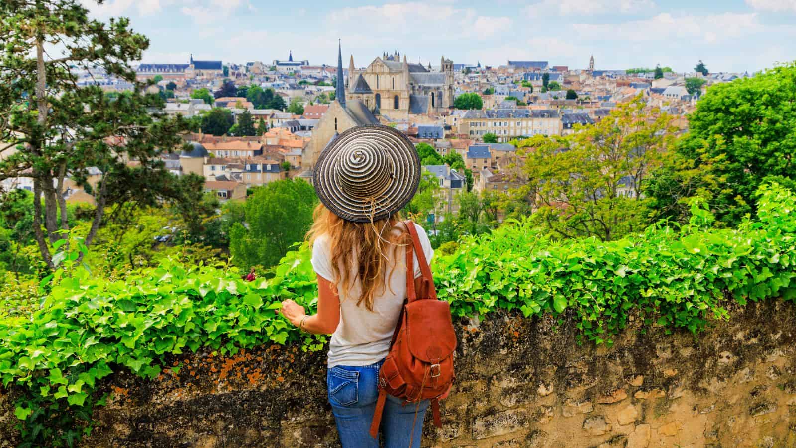 Charming woman with a sun hat overlooking historic European cityscape with lush greenery.