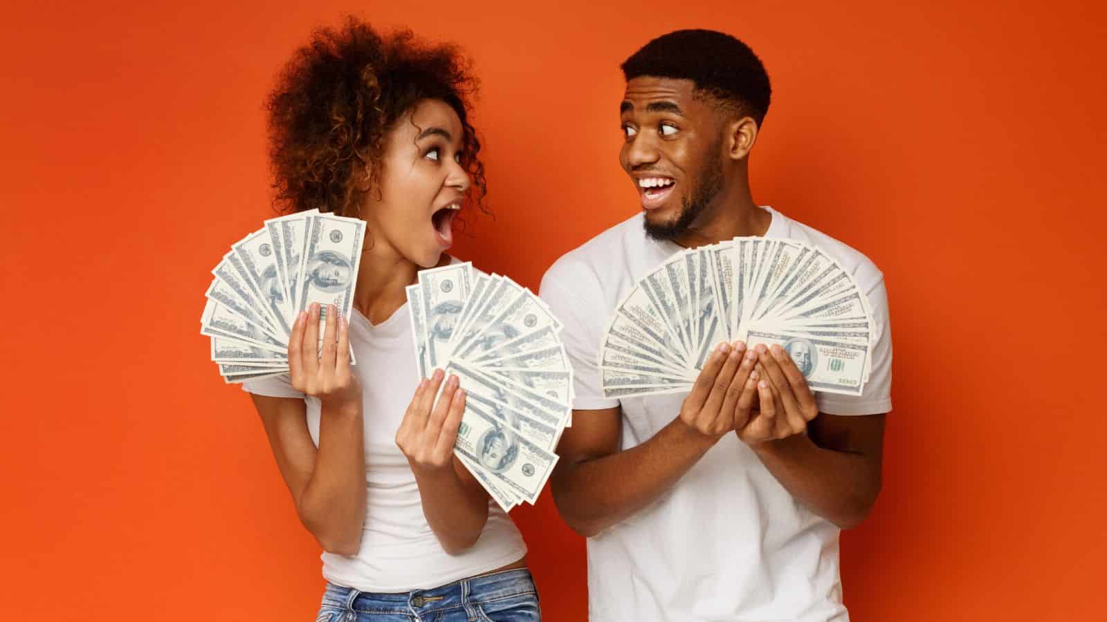 Two excited people holding and fanning out lots of cash against an orange background, ready to share their favorite ways to save money while you’re already on a cruise.