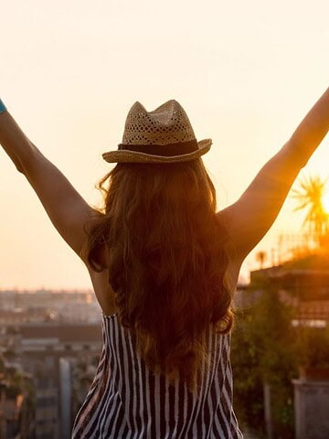 A girl raising both of her hands overlooking Italy.