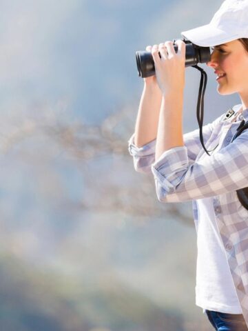 A girl smiling and looking through her binoculars.