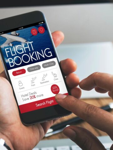 Person using a smartphone to book a flight online, with flight booking app visible on the screen.