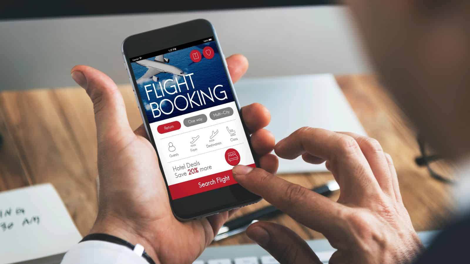 Person using a smartphone to book a flight online, with flight booking app visible on the screen.