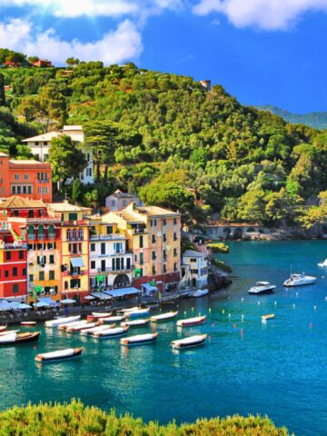 Colorful buildings and boats line the turquoise waterfront in a scenic Mediterranean coastal village.