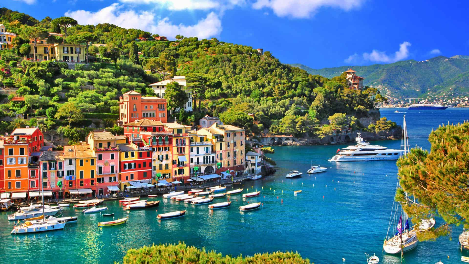 Colorful buildings and boats line the turquoise waterfront in a scenic Mediterranean coastal village.