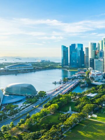 Aerial view of Singapore Marina Bay with skyscrapers, waterfront, and green park under blue sky.