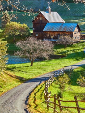 Winding country road leads to a rustic barn and pond surrounded by green fields and trees.