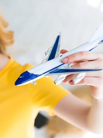 Woman in a yellow shirt smiling and holding a toy airplane, with a blurred background.