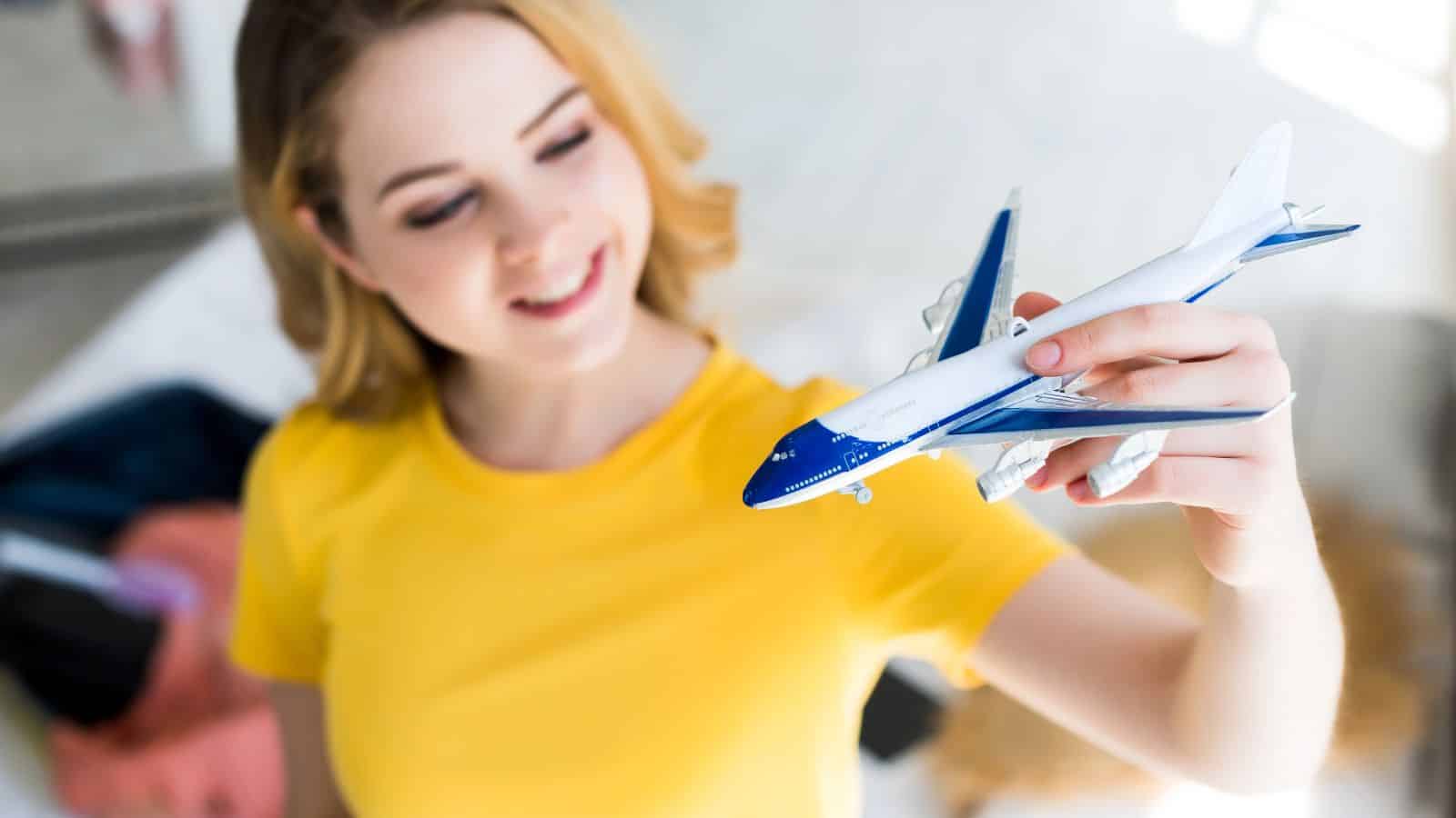 Woman in a yellow shirt smiling and holding a toy airplane, with a blurred background.
