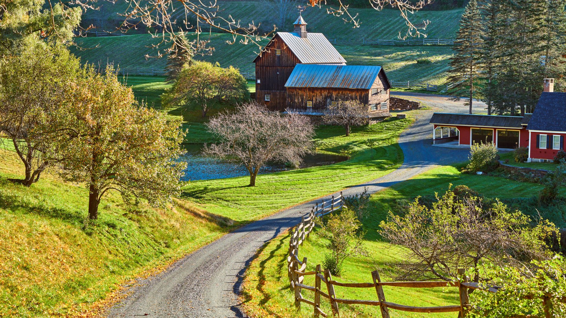Winding country road leads to a rustic barn and pond surrounded by green fields and trees.