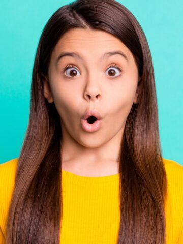 Girl with long brown hair in a yellow shirt looks surprised against a bright turquoise background, as if she just discovered some bizarre holidays celebrated in the top 10 states.