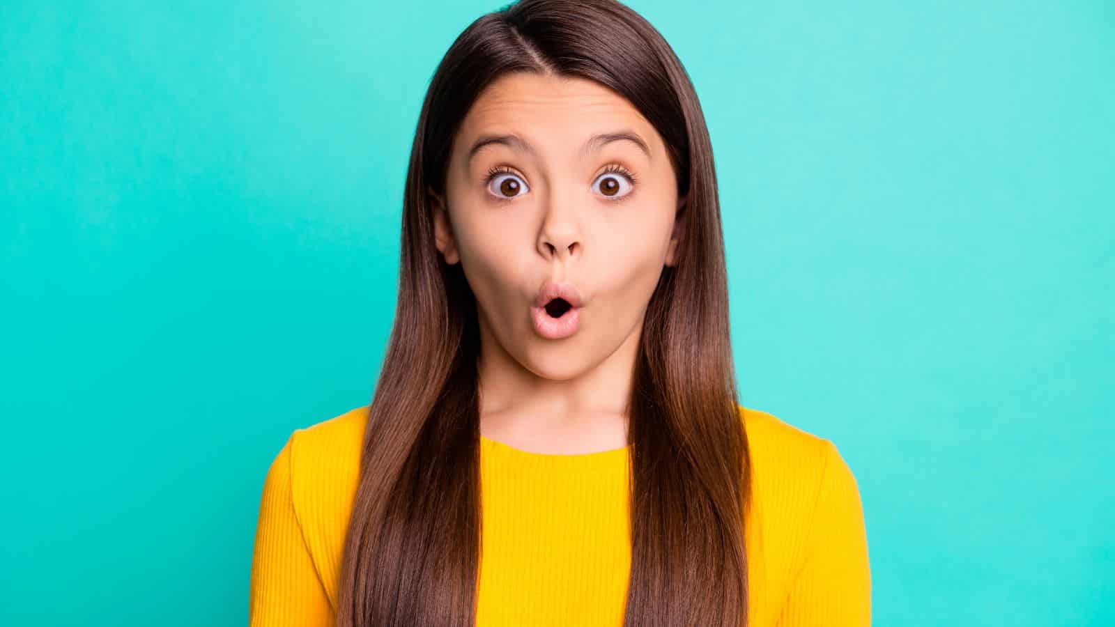 Girl with long brown hair in a yellow shirt looks surprised against a bright turquoise background, as if she just discovered some bizarre holidays celebrated in the top 10 states.