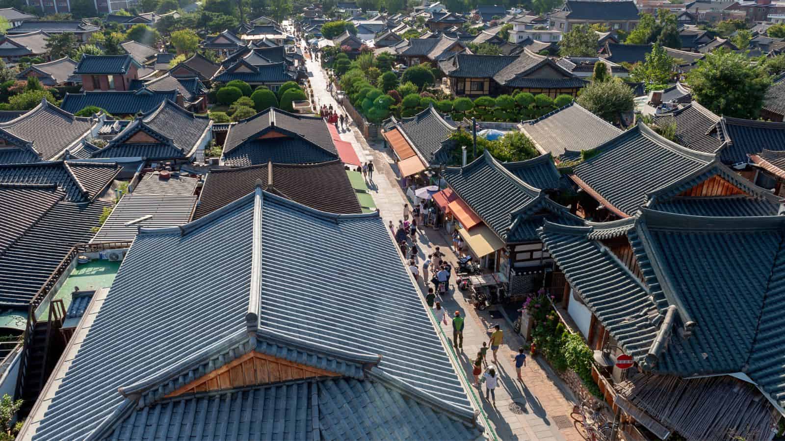 Aerial view of a traditional Korean village with tiled rooftops, narrow streets, and people walking.