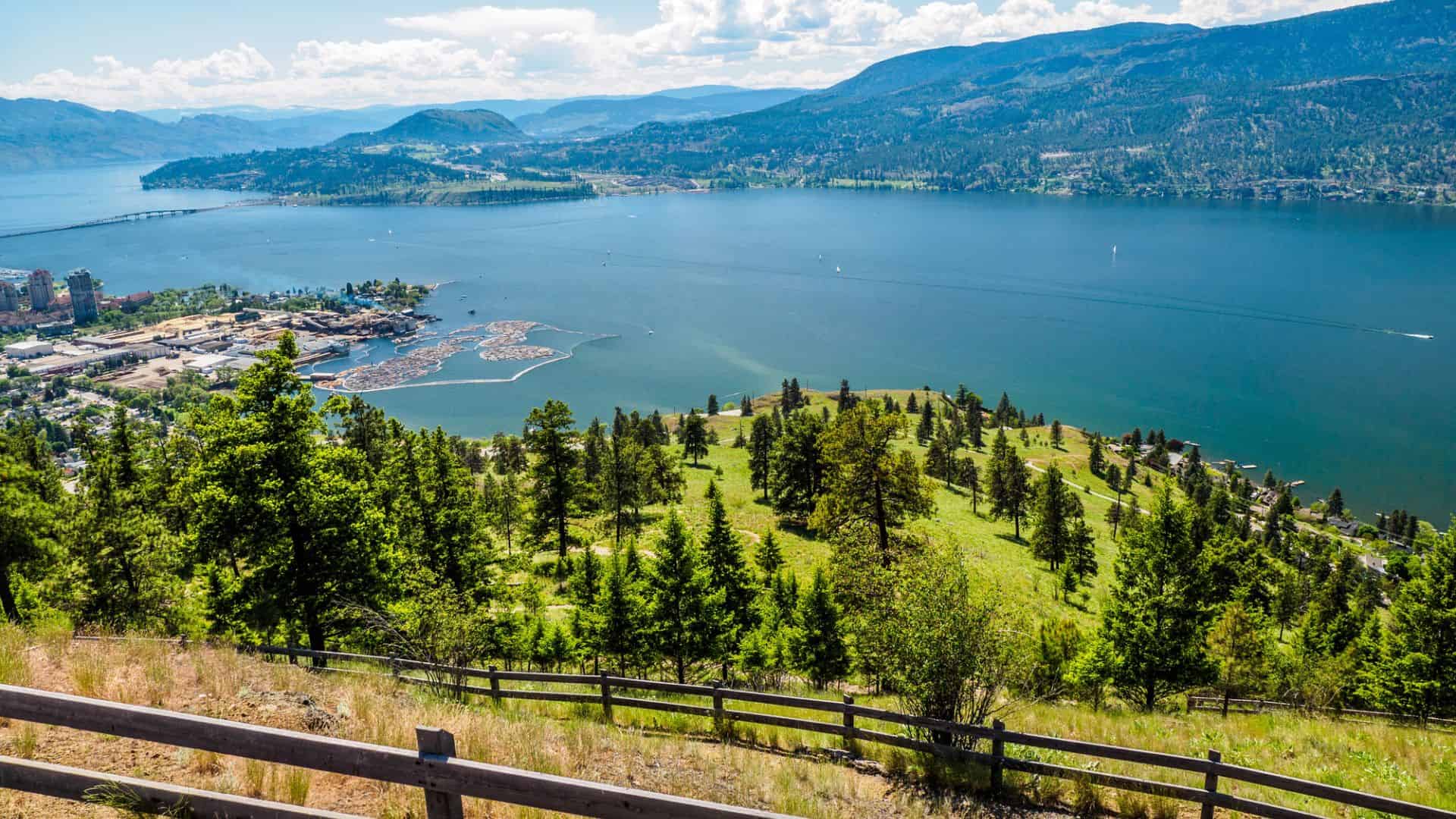 Overlooking a lake surrounded by green hills, trees, and a distant town under a partly cloudy sky.
