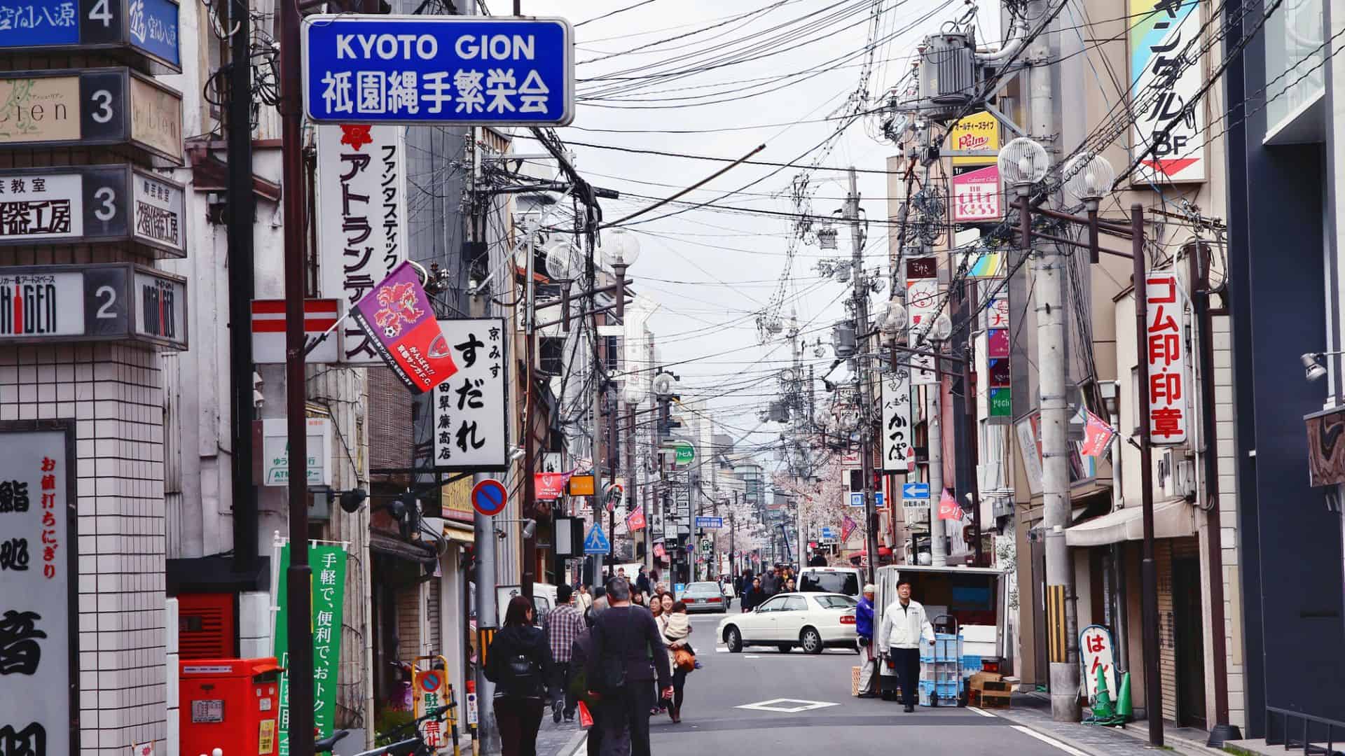 Busy street in Kyoto, Japan with shops, signs, power lines, and people walking in both directions.
