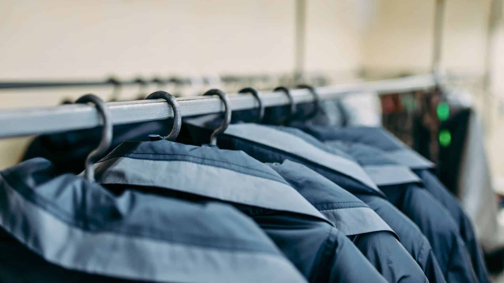 Close-up of several dark-colored jackets hanging on a metal clothing rack with hangers.