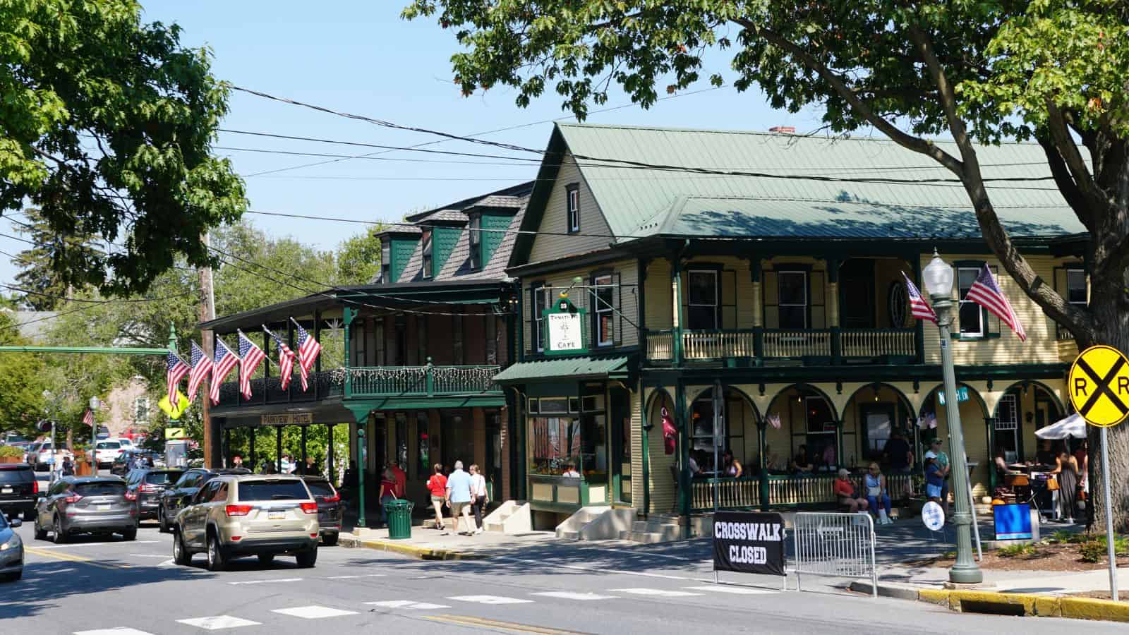 Busy small-town street adorned with historic buildings, American flags, and cars, as a "Crosswalk Closed" sign marks the scene—perfect for an autumn travel snapshot of classic small towns.