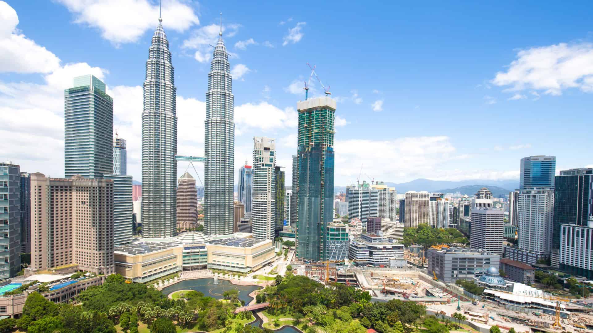 Kuala Lumpur skyline with the Petronas Twin Towers and city buildings under a bright blue sky.