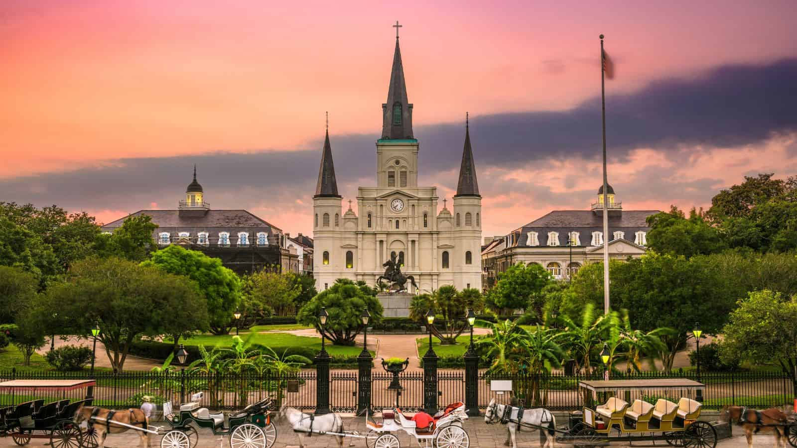 St. Louis Cathedral in New Orleans at sunset, with horse-drawn carriages lined up in front.