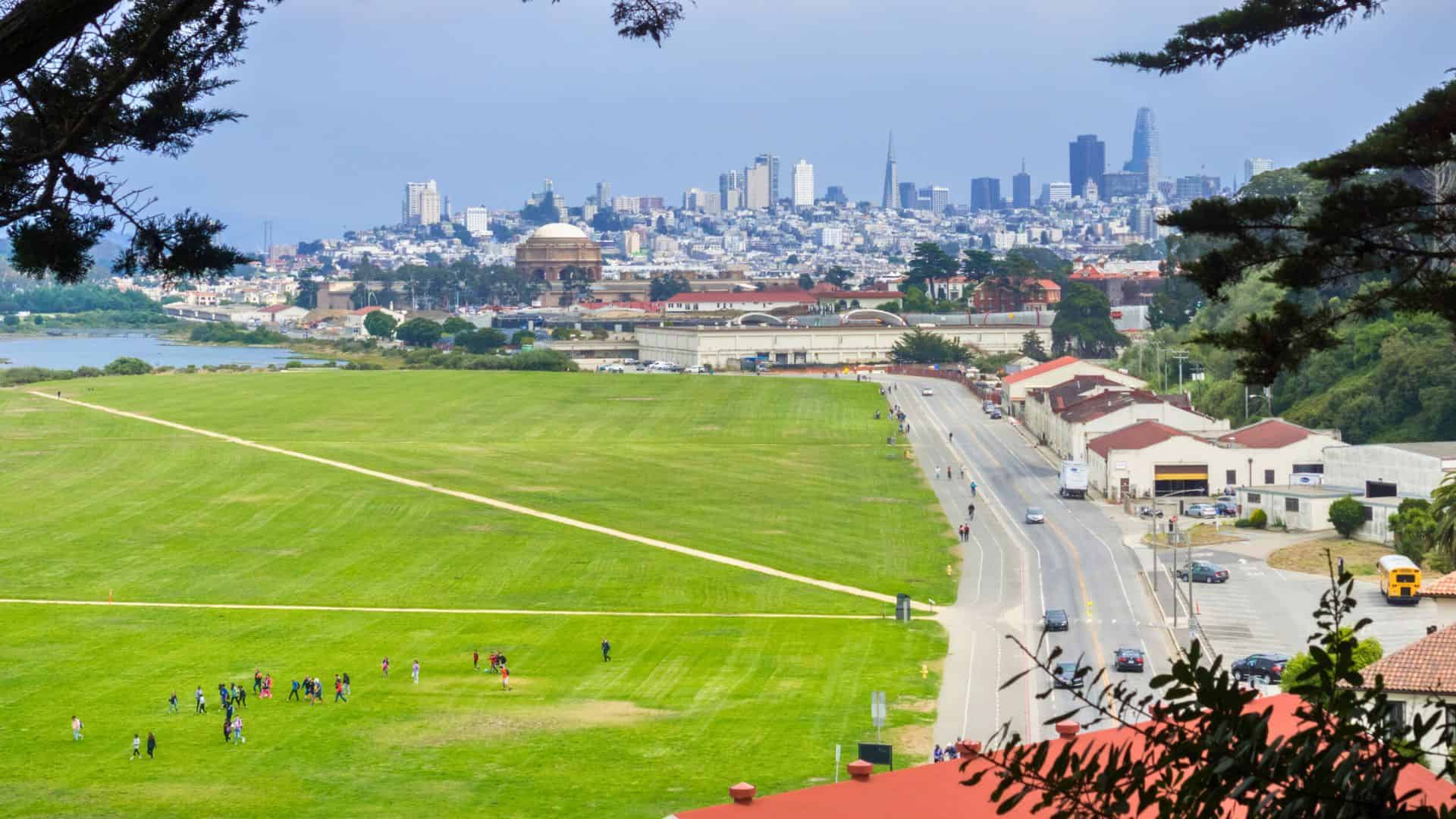 View of a large green park with people, city buildings, and the San Francisco skyline in the background.