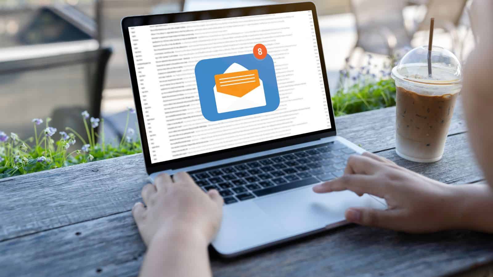 Person using laptop outdoors, email inbox on screen shows 8 new messages, iced coffee next to computer.