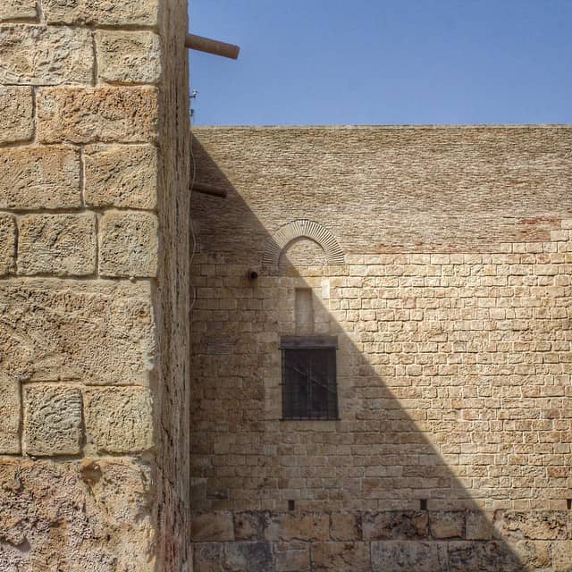 Sunlit stone wall with a small arched window and a shadow creating a diagonal line&mdash;perfect inspiration when considering what to do in Palermo for a day, capturing the city's historic charm in a single frame.