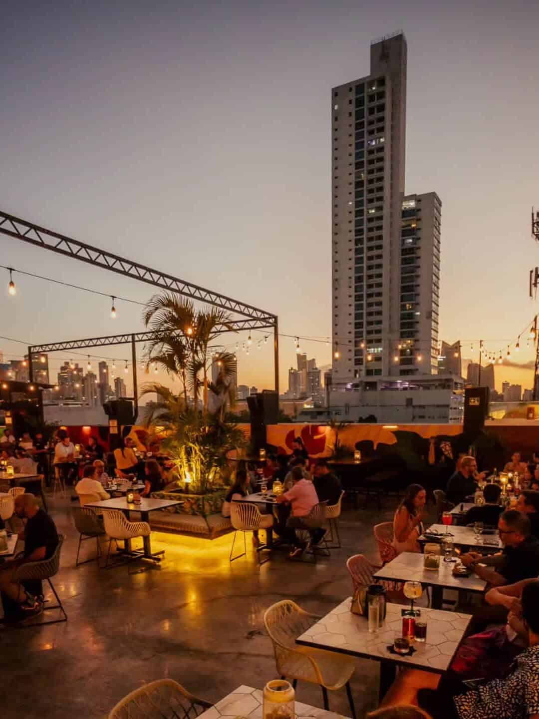Rooftop restaurant at sunset with diners, string lights, city buildings, and a tall skyscraper in the background&mdash;one of the best restaurants in Barcelona for those seeking unforgettable views.