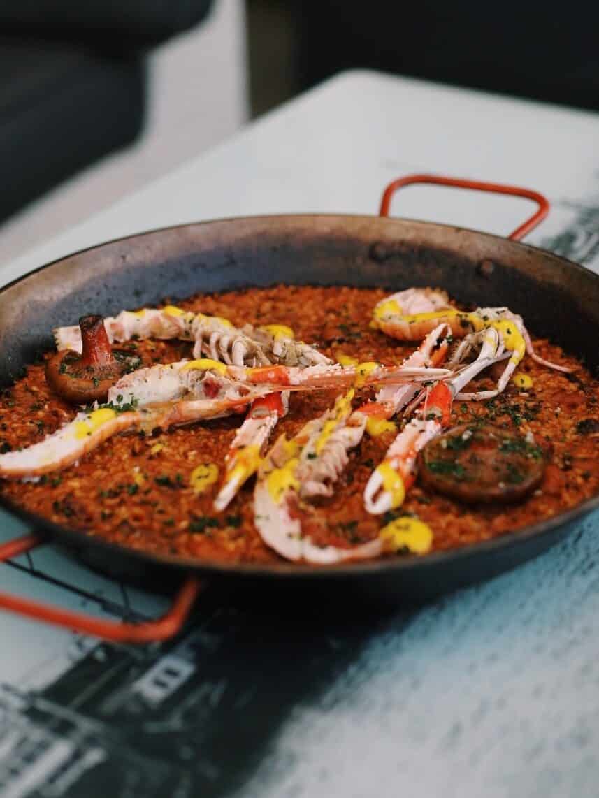 A pan of seafood paella with crab legs, garnished with herbs and sauce, on a white table—a favorite at some of the best restaurants Barcelona has to offer.