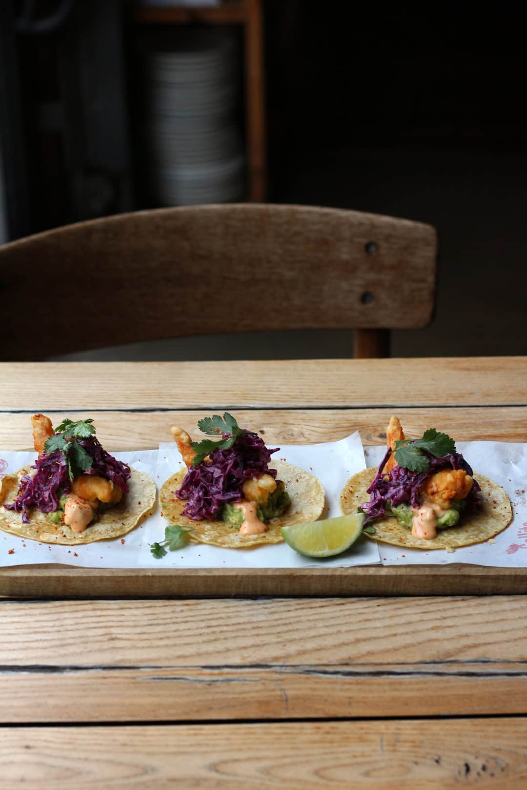 Three fish tacos topped with purple slaw and cilantro on a wooden table, with a lime wedge on the side—a flavorful taste of Barcelona dining.