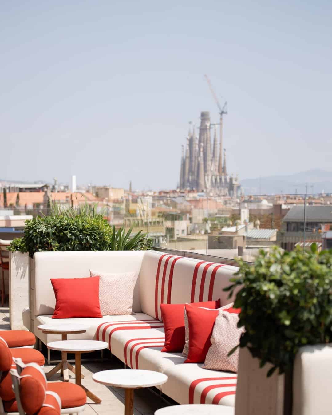Rooftop lounge with red-striped cushions overlooking Barcelona and La Sagrada Fam&iacute;lia in the distance&mdash;one of the standout Barcelona restaurants with a view.