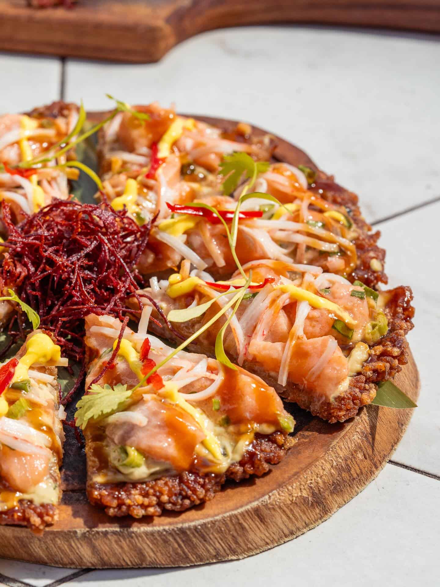 Sliced sushi pizza topped with salmon, sprouts, herbs, and sauces on a wooden serving board&mdash;perfect for those seeking unique flavors in Barcelona restaurants.