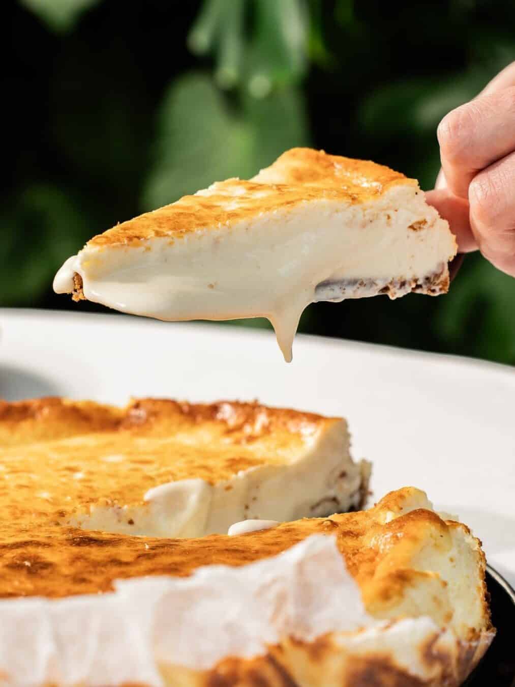 A hand lifts a creamy slice of cheesecake from a whole cheesecake on a table, perfect for indulging after exploring the Best Restaurants in Barcelona.