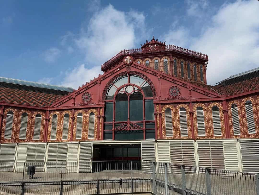 Red and gold ornate building with arched windows and intricate details under a partly cloudy sky, reminiscent of the vibrant atmosphere found in Barcelona markets where to eat fresh food is a daily delight.