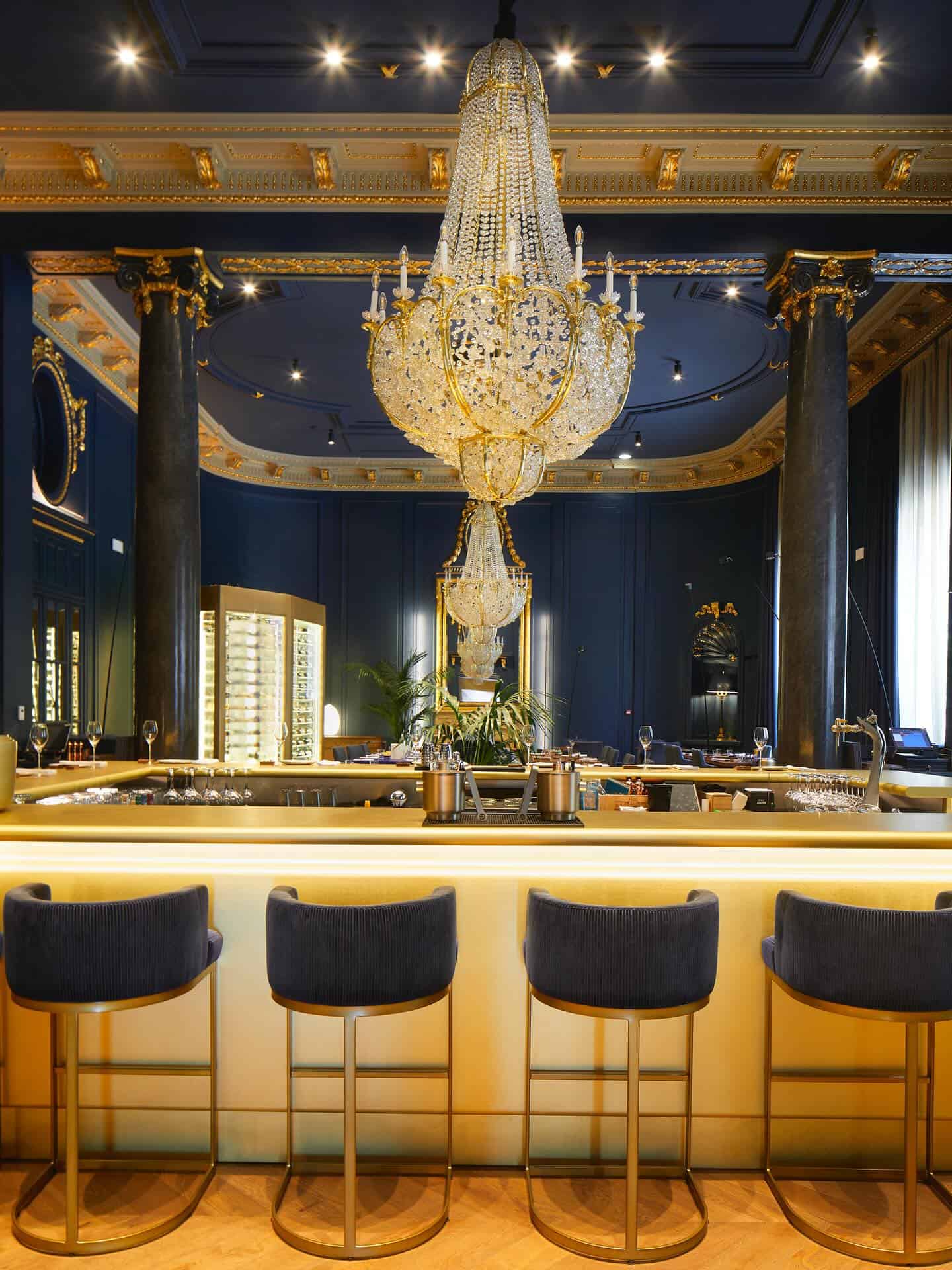 Luxurious bar with gold accents, velvet bar stools, and a large, ornate crystal chandelier overhead&mdash;perfect for those seeking the Best Restaurants in Barcelona or featured in any Barcelona Guide.