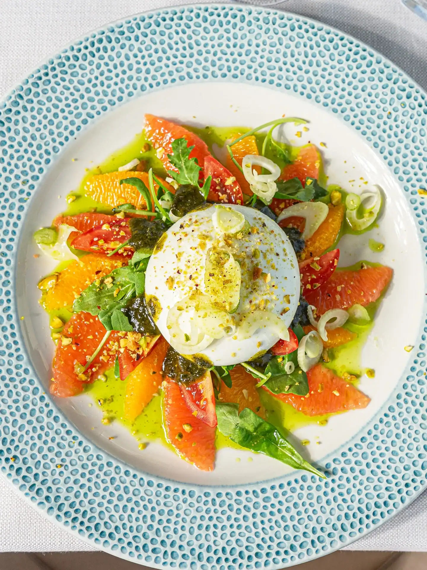 Enjoy a plate of burrata cheese with citrus slices, greens, pistachios, and green oil&mdash;an artful dish often found at the best restaurants in Barcelona.
