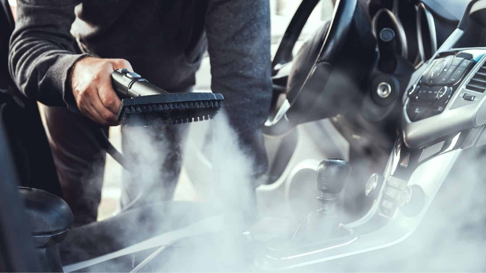Person steam cleaning the interior of a car, with steam rising near the gear shift and dashboard.